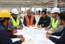 Equipe diversificada de profissionais trabalhando em um canteiro de obras moderno, com engenheira, arquiteto, técnico e operários analisando projetos e tecnologia BIM.