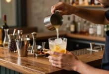 Bartender preparando um drink profissional com coqueteleira, frutas cítricas, gelo e utensílios de bar em um ambiente elegante