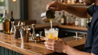 Bartender preparando um drink profissional com coqueteleira, frutas cítricas, gelo e utensílios de bar em um ambiente elegante