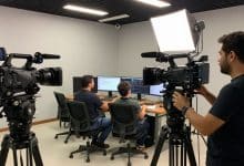 Equipe em um estúdio audiovisual prepara uma gravação com câmera, iluminação e monitor, representando diferentes carreiras do setor.