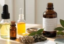 Frascos de óleos essenciais e folhas aromáticas sobre uma mesa clara, compondo uma cena acolhedora de estudo de aromaterapia.